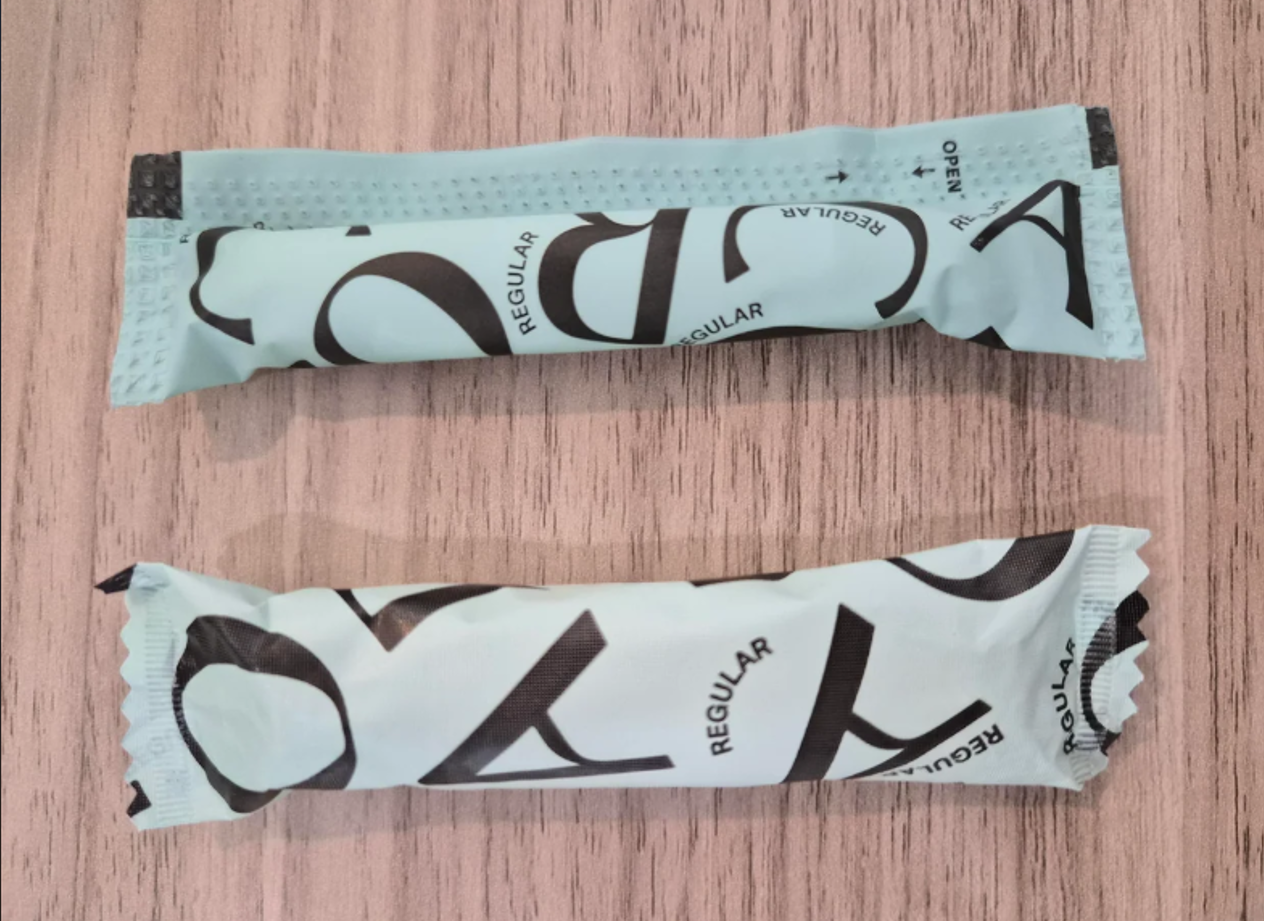 Two teal-colored, rectangular packets labeled "REGULAR" in black text lie on a wooden surface. The packets are crimped at the edges and appear unopened, reminiscent of photos of shrinking products often seen in discussions about changing package sizes.