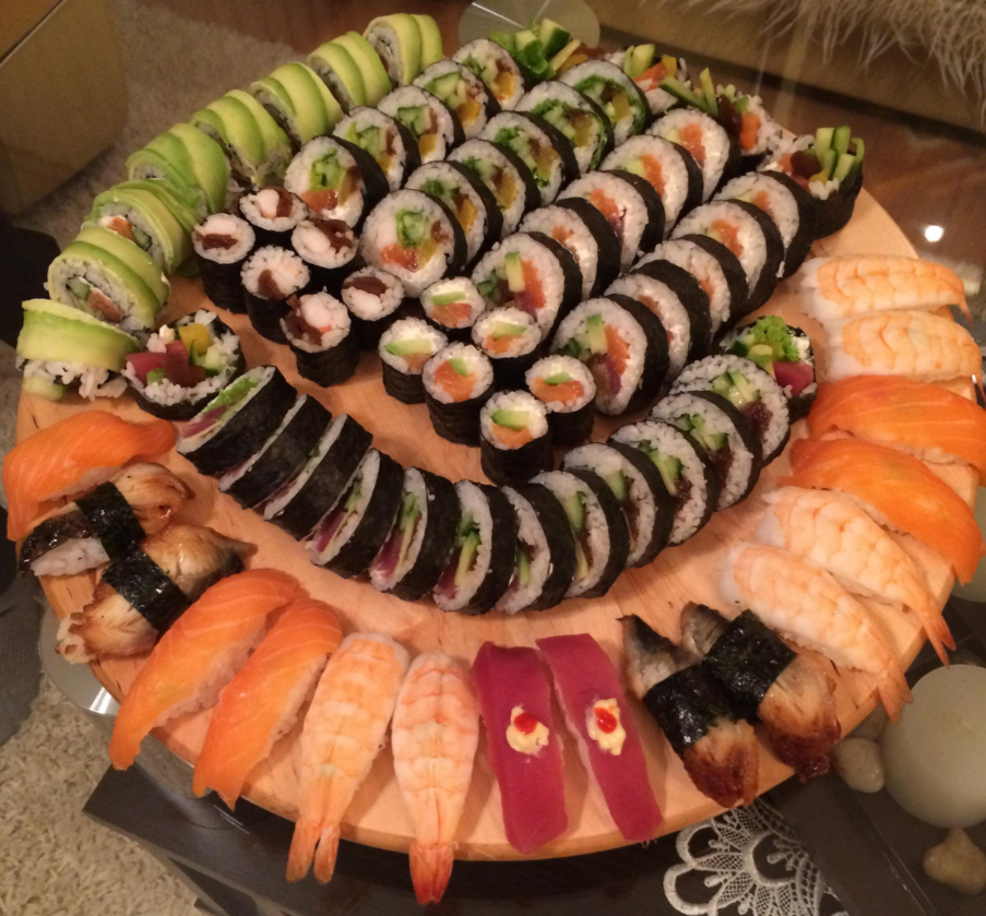 A large wooden platter filled with assorted sushi rolls, nigiri with salmon, shrimp, eel, and tuna, arranged in neat, colorful rows.