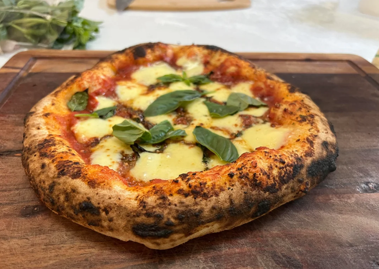 A freshly baked margherita pizza with melted cheese, tomato sauce, and fresh basil leaves sits on a wooden cutting board.