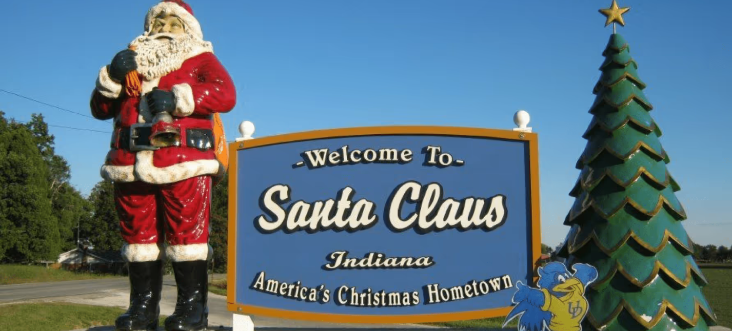 A statue of Santa Claus stands next to a large welcome sign and a Christmas tree in Santa Claus, Indiana, proudly showcasing its tagline “America’s Christmas Hometown”—a fitting title for one of the best Christmas towns in America.