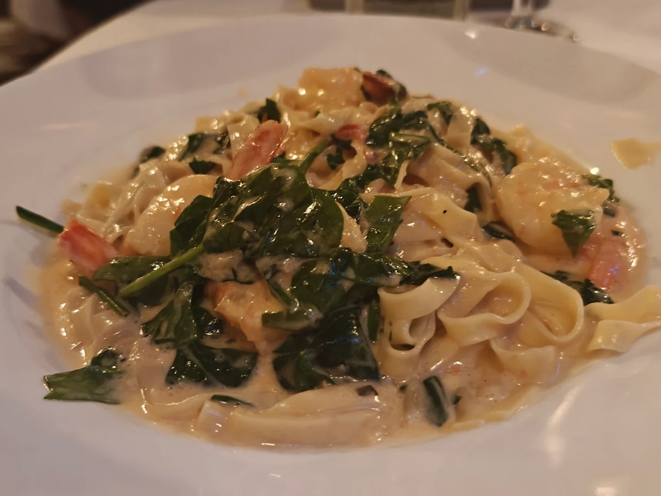 A plate of creamy fettuccine pasta with shrimp and spinach, served in a white sauce, garnished with herbs on a white dish.