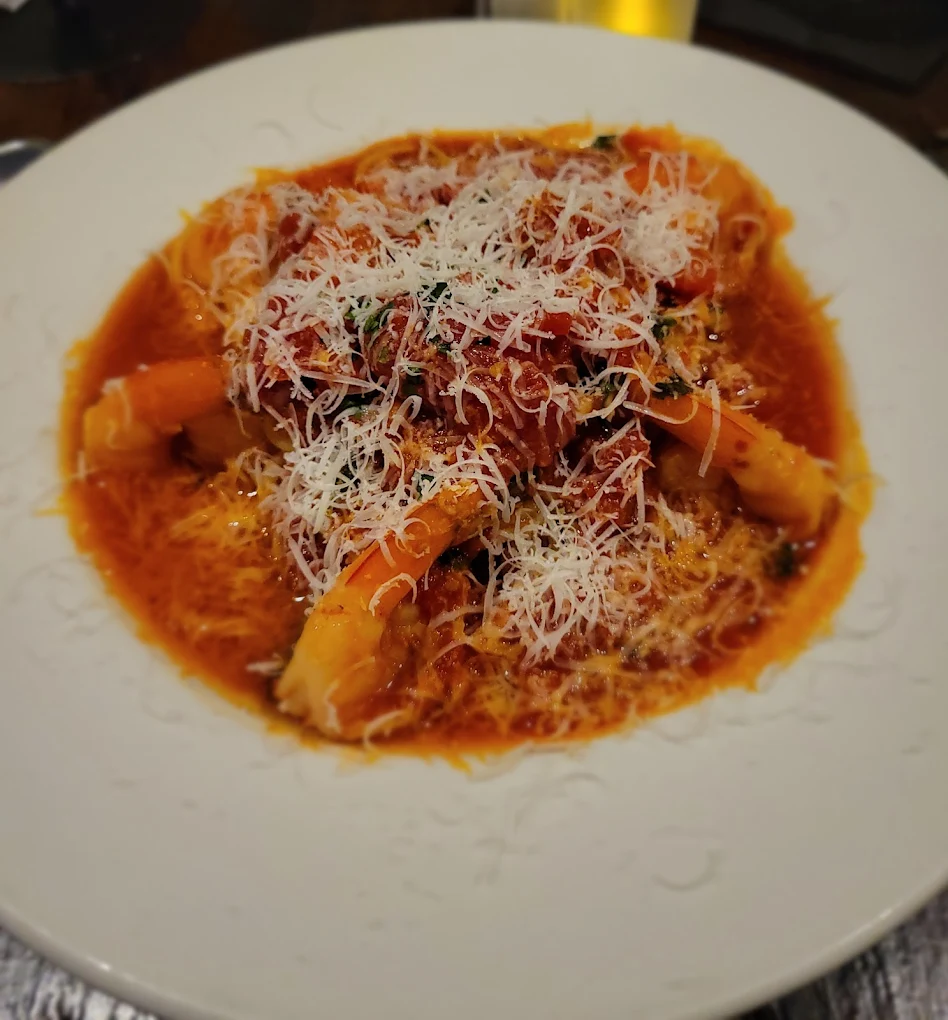 A white plate filled with pasta in a rich red tomato sauce, topped with grated cheese and garnished with herbs. The dish appears warm and freshly served.