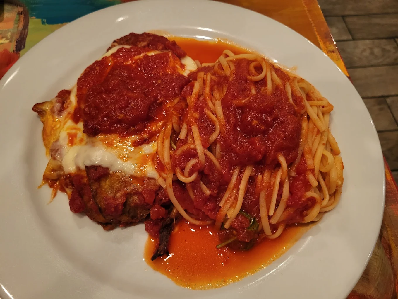 A white plate with a serving of spaghetti topped with marinara sauce beside eggplant parmesan covered in melted cheese and red sauce.