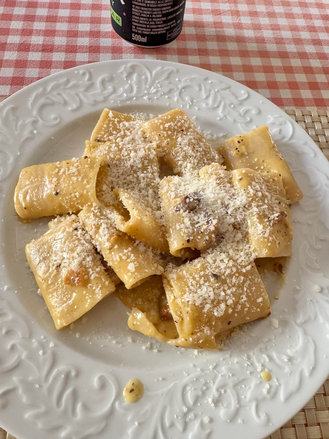 A white plate of pasta with a creamy sauce and grated cheese on top, sitting on a pink and white checkered tablecloth.