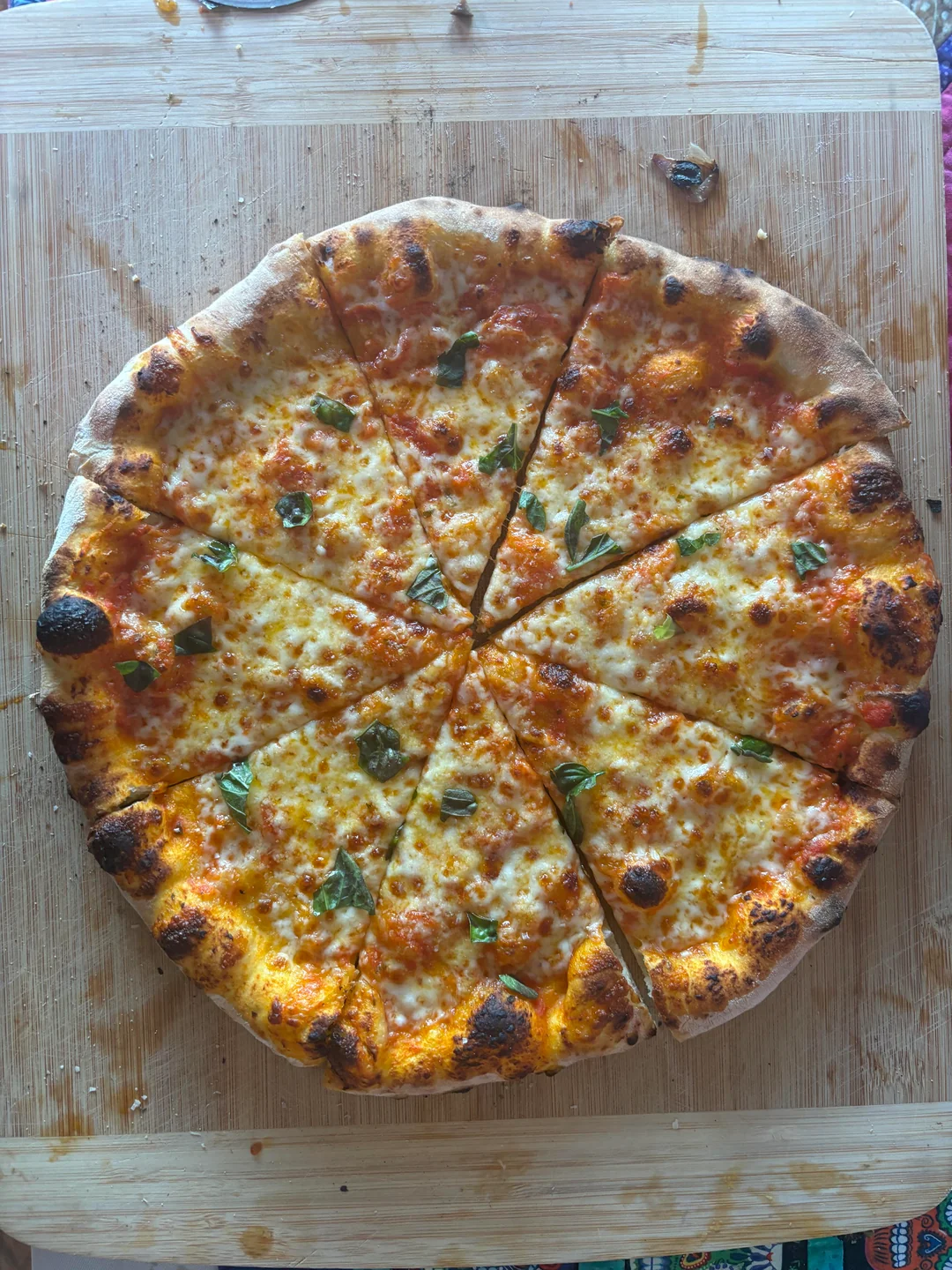 A whole pizza topped with melted cheese and fresh basil is sliced into eight pieces and placed on a wooden cutting board.