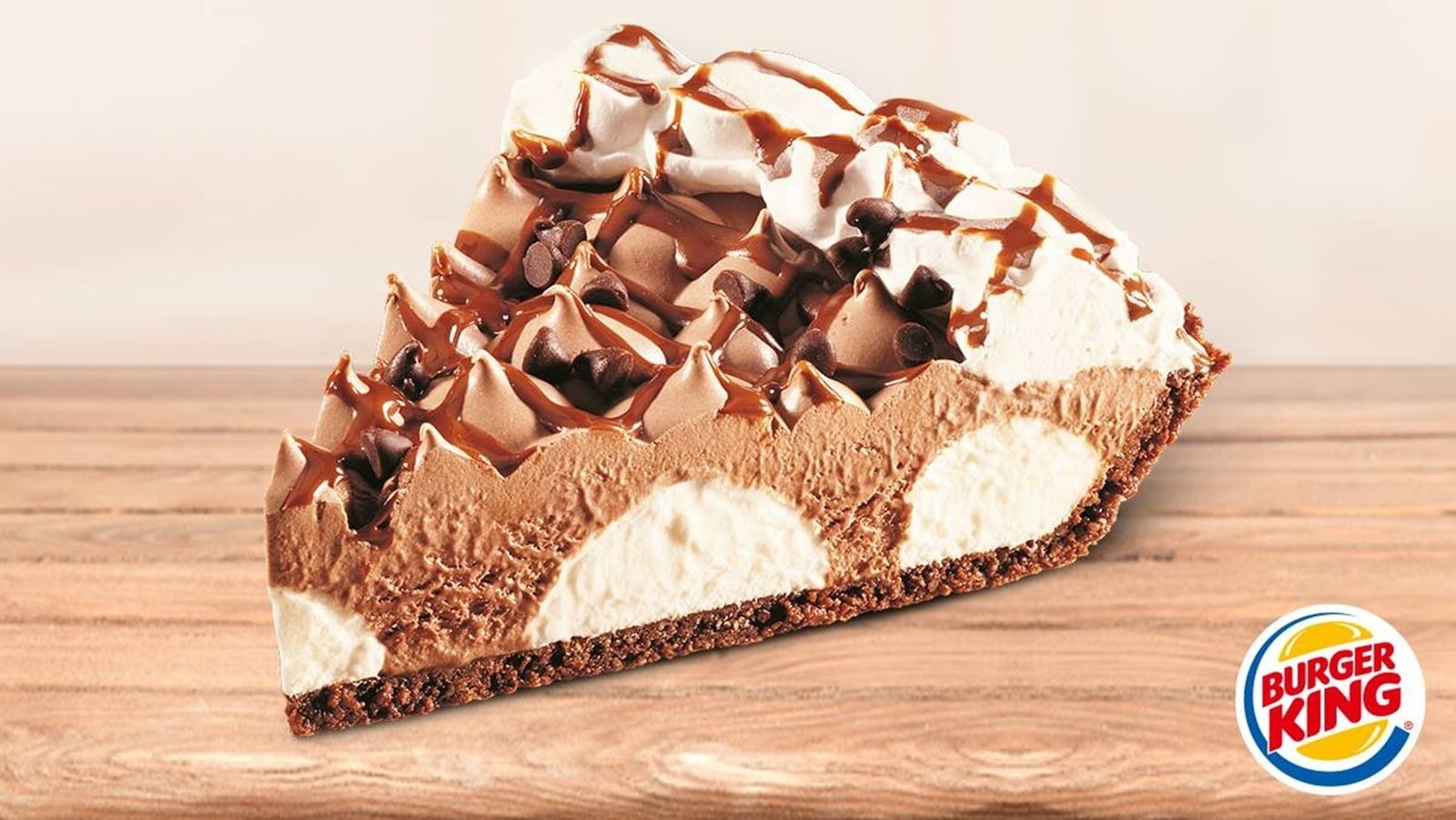 A slice of chocolate cream pie with whipped topping, chocolate drizzle, and chocolate chips sits on a wooden surface. The Burger King logo appears in the lower right corner.