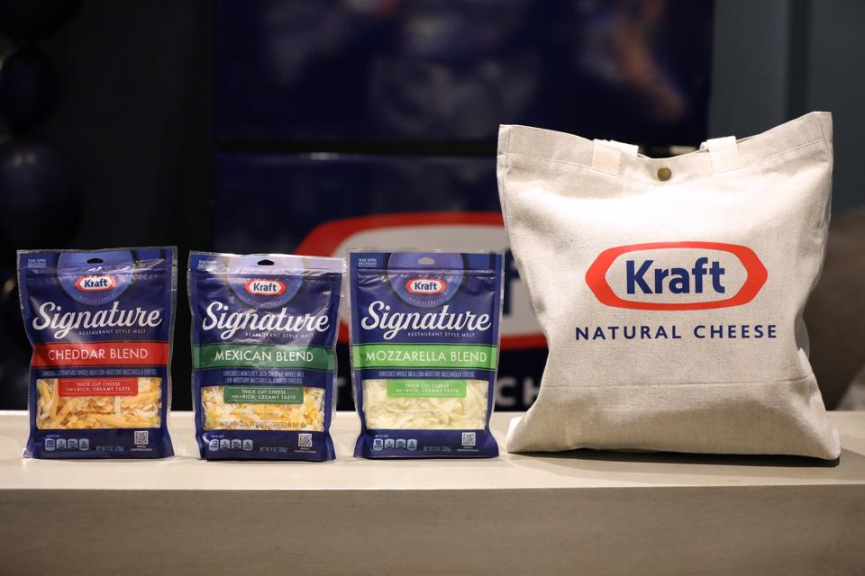 Three Kraft Signature shredded cheese bags (Cheddar Blend, Mexican Blend, Mozzarella Blend) are displayed next to a beige Kraft Natural Cheese tote bag on a counter.