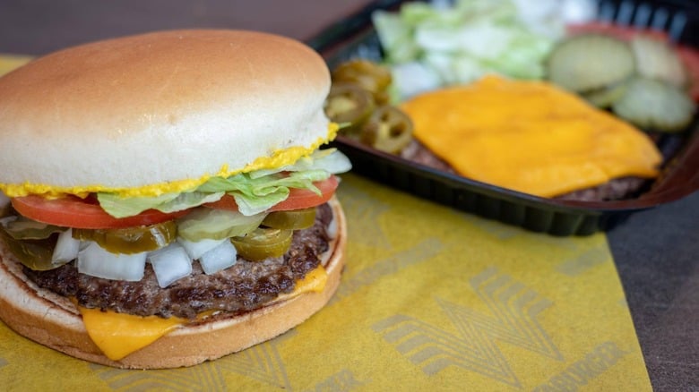 A cheeseburger with lettuce, tomato, pickles, onions, and jalapeños sits on a Whataburger wrapper next to an open container holding a deconstructed cheeseburger with cheese, lettuce, pickles, and onions.
