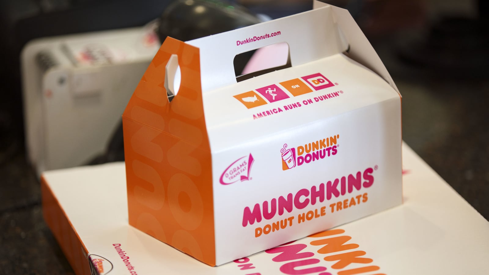 A Dunkin' Donuts Munchkins box, labeled "Munchkins Donut Hole Treats," sits on a counter. The box features orange and pink branding and the Dunkin' Donuts logo.