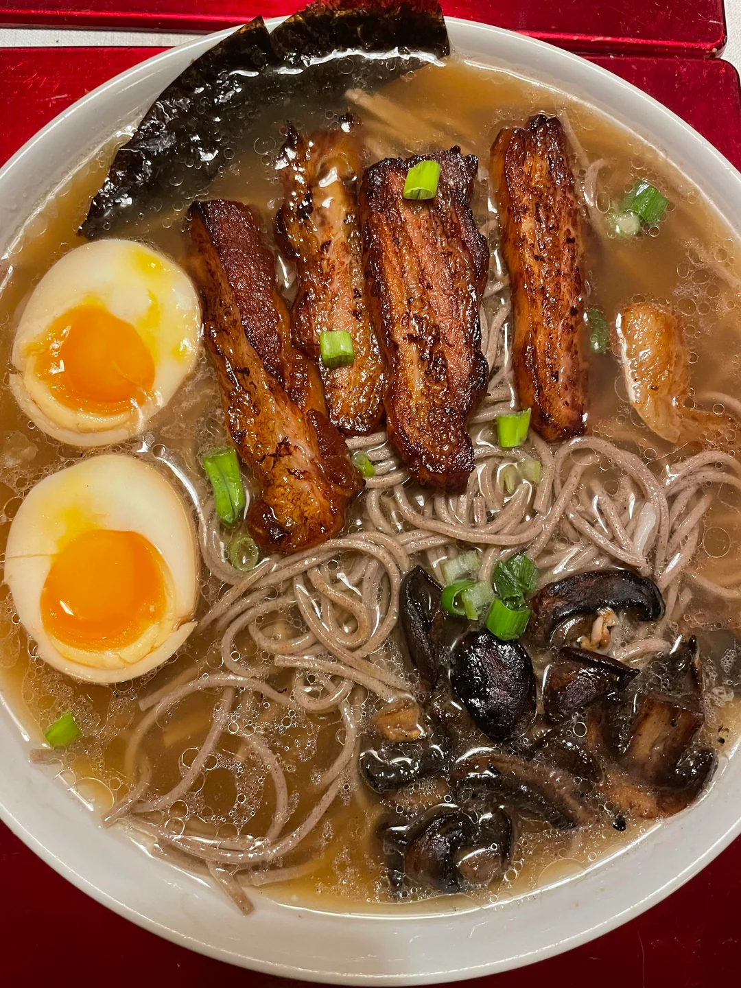 A bowl of ramen with soft-boiled eggs, grilled pork belly slices, nori seaweed, mushrooms, green onions, and noodles in broth.