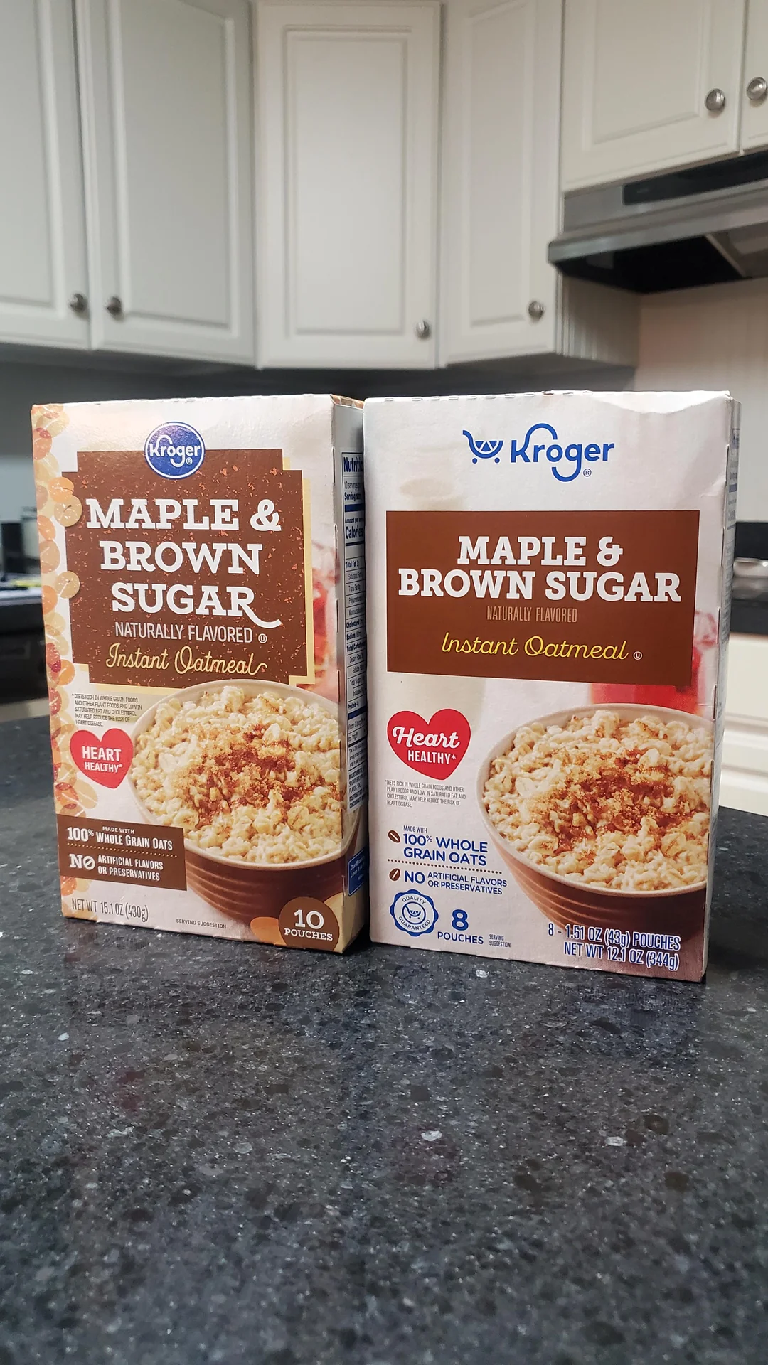 Two boxes of Kroger Maple & Brown Sugar Instant Oatmeal are on a kitchen counter. Each box features a bowl of oatmeal on the front. Cabinets, a stove, and a kitchen backsplash appear in the background.