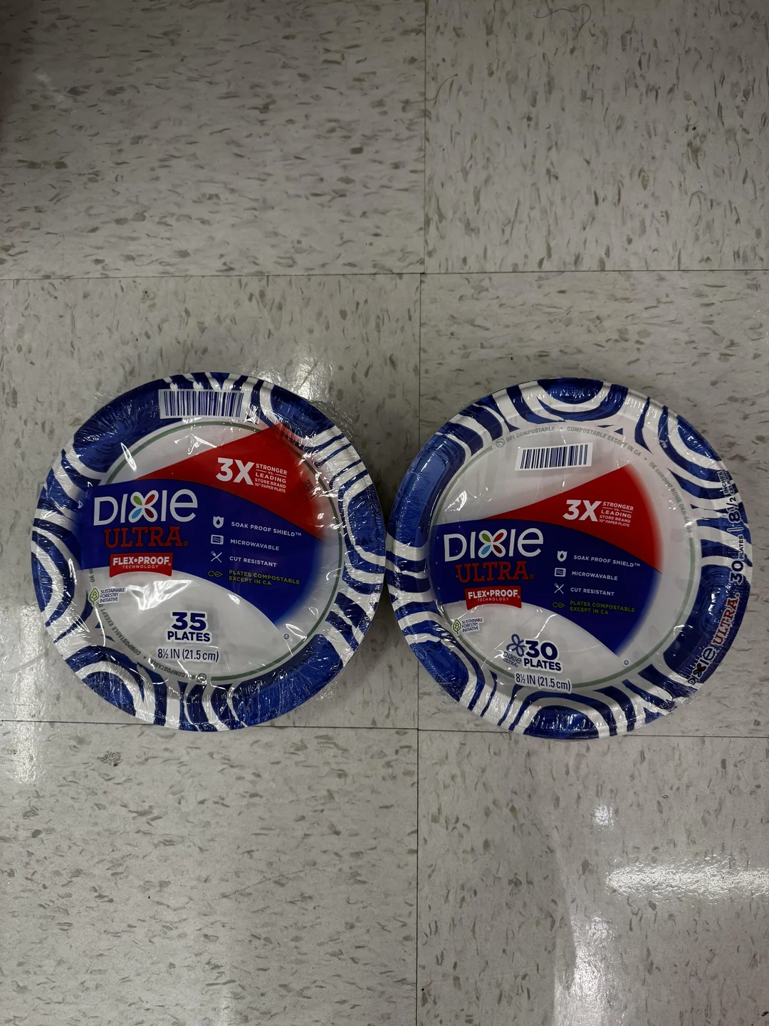 Two packs of Dixie Ultra disposable plates on a white floor: the left pack has 35 plates, and the right pack has 30 plates. Both packs have a blue and red design with white accents.