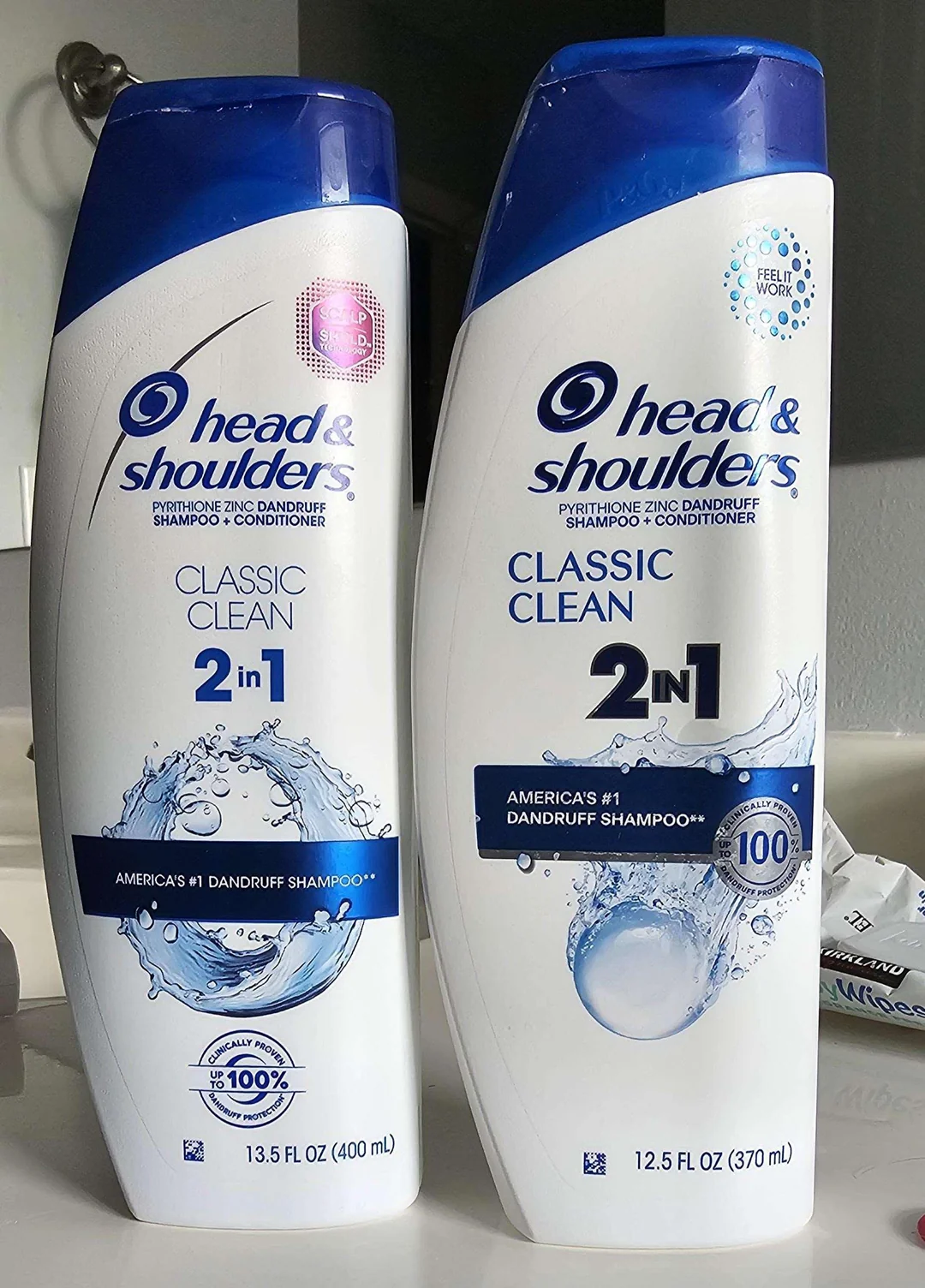Two bottles of Head & Shoulders Classic Clean 2-in-1 shampoo and conditioner sit side by side on a counter, one 13.5 fl oz (400 mL) and the other 12.5 fl oz (370 mL).