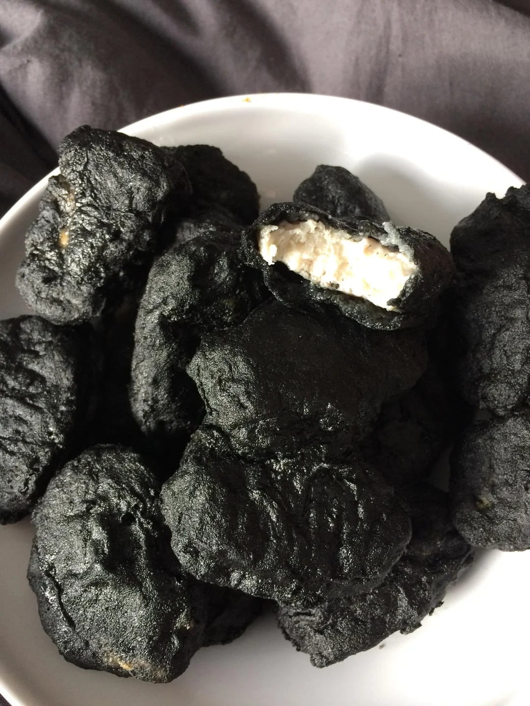 A bowl filled with several black-colored nuggets, one of which is broken open to reveal a white filling inside.