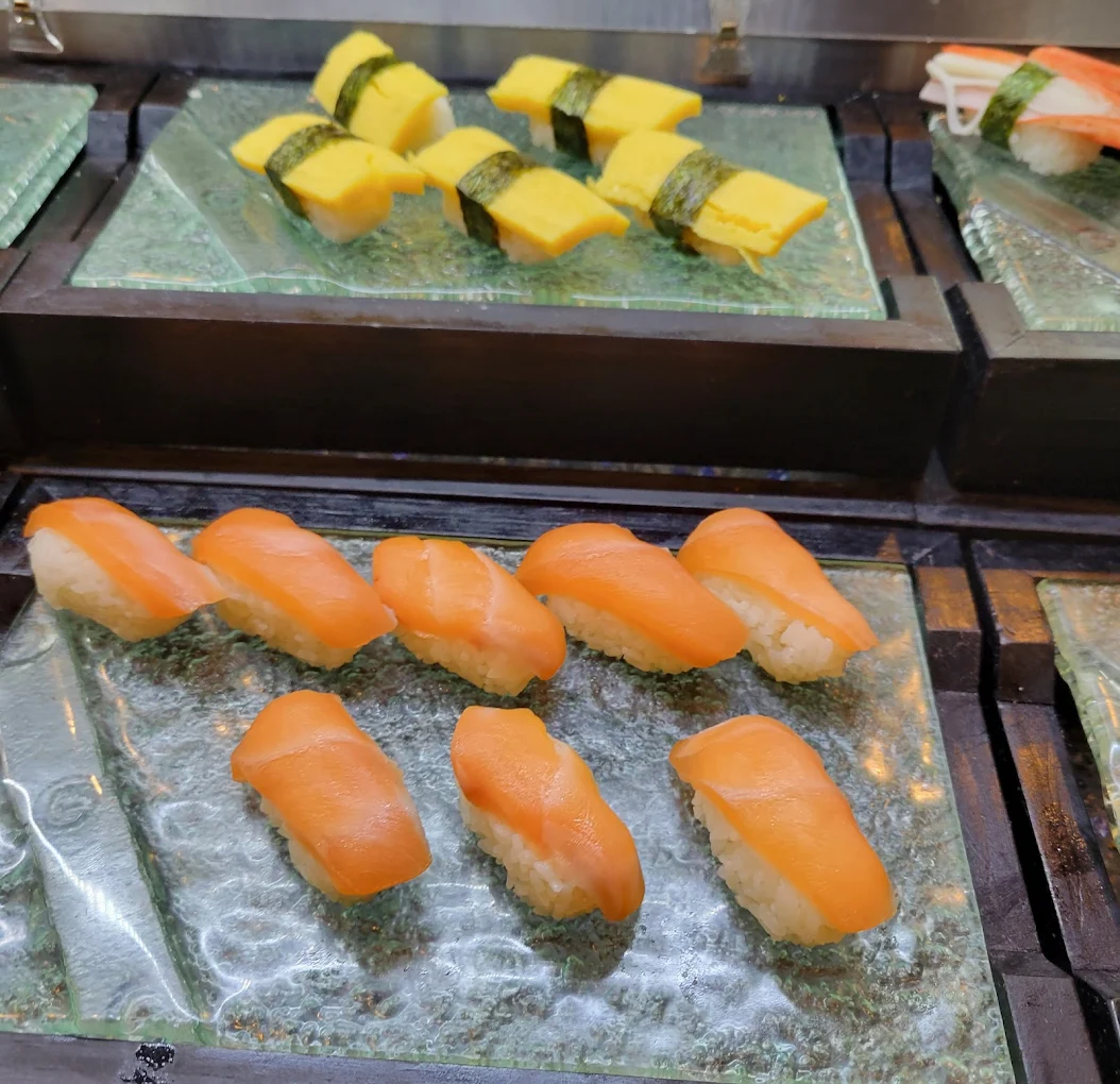 A display of sushi on glass plates, featuring pieces of salmon nigiri in the front and tamago (egg) nigiri wrapped with seaweed in the back.