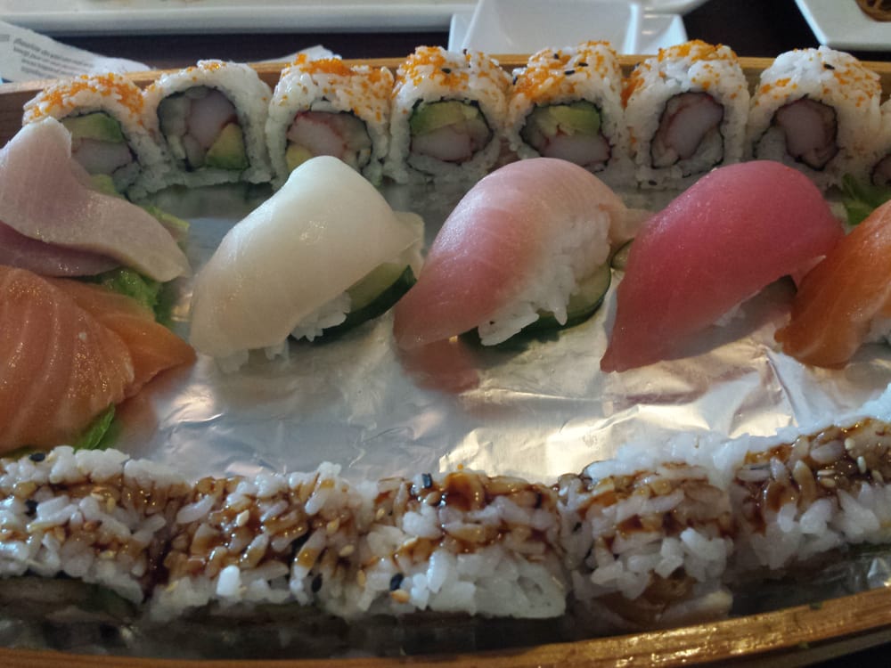 A platter of assorted sushi, including rolls topped with orange roe, nigiri with various fish slices, and rolls drizzled with dark sauce, arranged on a foil-covered tray.