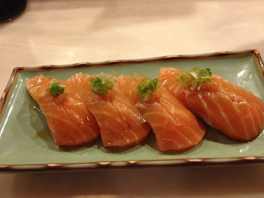 Four pieces of salmon nigiri sushi topped with chopped green onions are neatly arranged on a rectangular green ceramic plate.