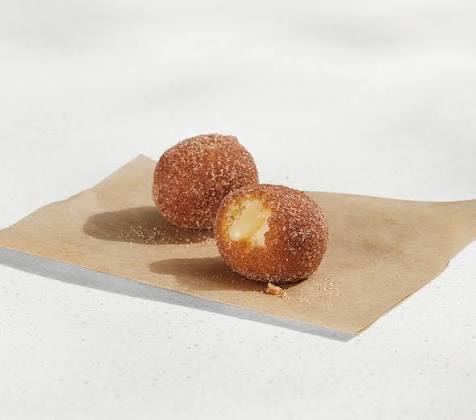 Two round, sugar-coated doughnuts sit on a piece of brown paper. One doughnut is whole, while the other is bitten, revealing a creamy yellow filling inside.
