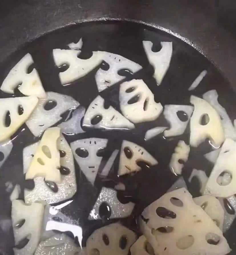 Sliced lotus root pieces floating in water. The holes in the slices make them resemble cartoon faces with various expressions.