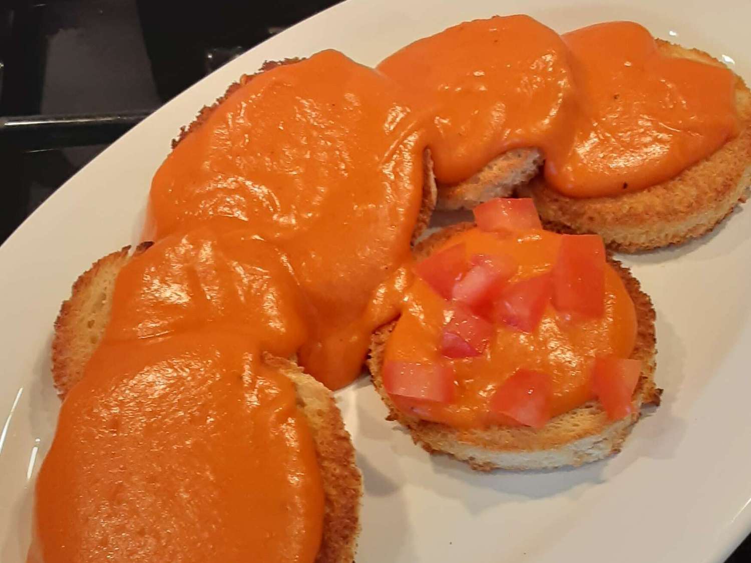 Toasted bread rounds topped with melted orange cheese sauce, served on a white plate. One toast is garnished with small diced tomatoes.