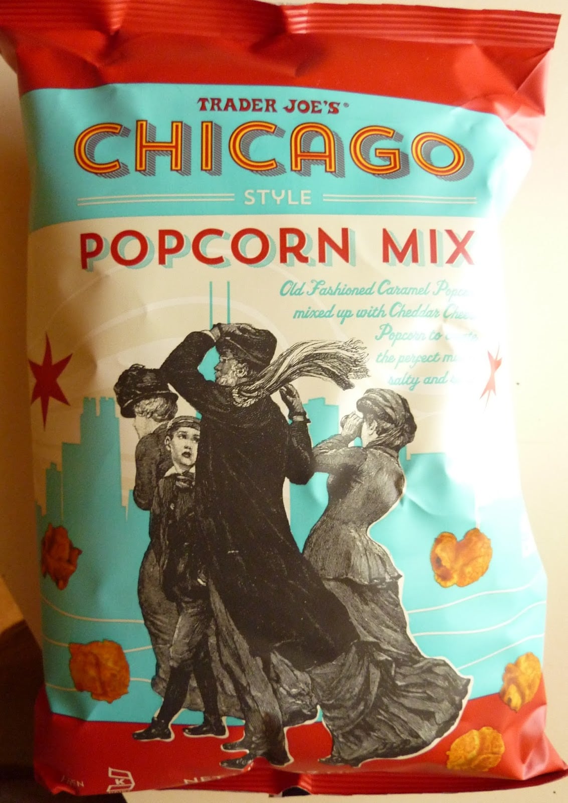 Bag of Trader Joe’s Chicago Style Popcorn Mix, featuring illustrations of people in vintage clothing blown by wind, with popcorn pieces and a city skyline in the background.