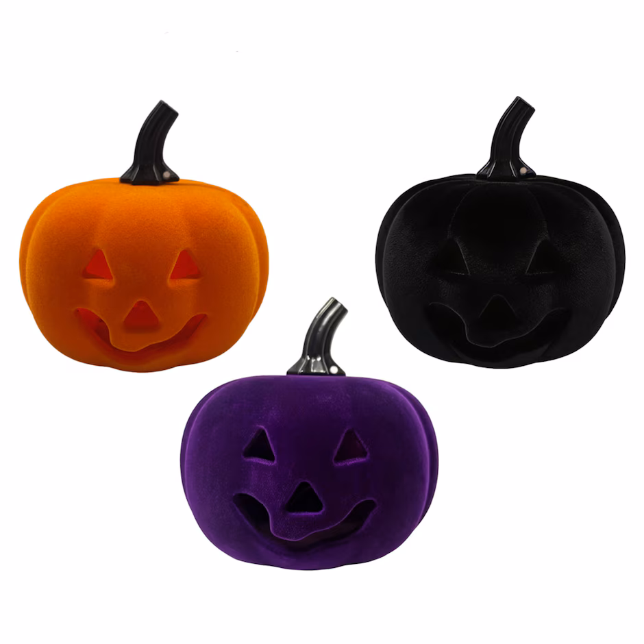 Three velvet pumpkins—orange, black, and purple—each with a carved jack-o’-lantern smile and triangular eyes, are displayed on a white background.