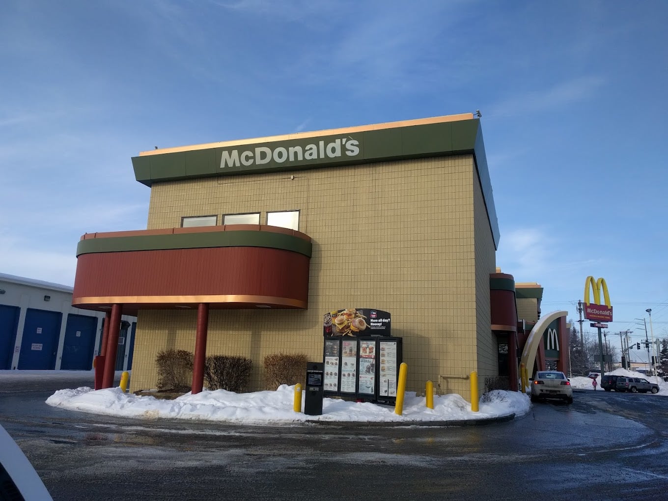 A McDonald's restaurant, one of the favorite fast-food chains by state, with a drive-thru menu board in a snowy parking lot under a clear blue sky. The building features an unusual design, and the classic golden arches sign is visible in the background.