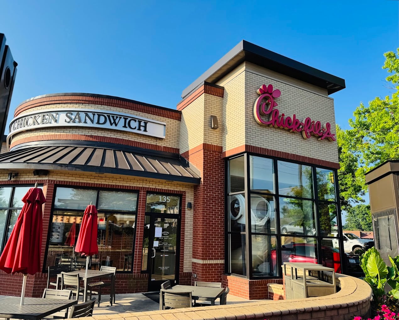 A Chick-fil-A restaurant with outdoor seating, red umbrellas, large windows, and clear signage stands out as one of the favorite fast-food chains by state. The sky is blue and trees are visible in the background.