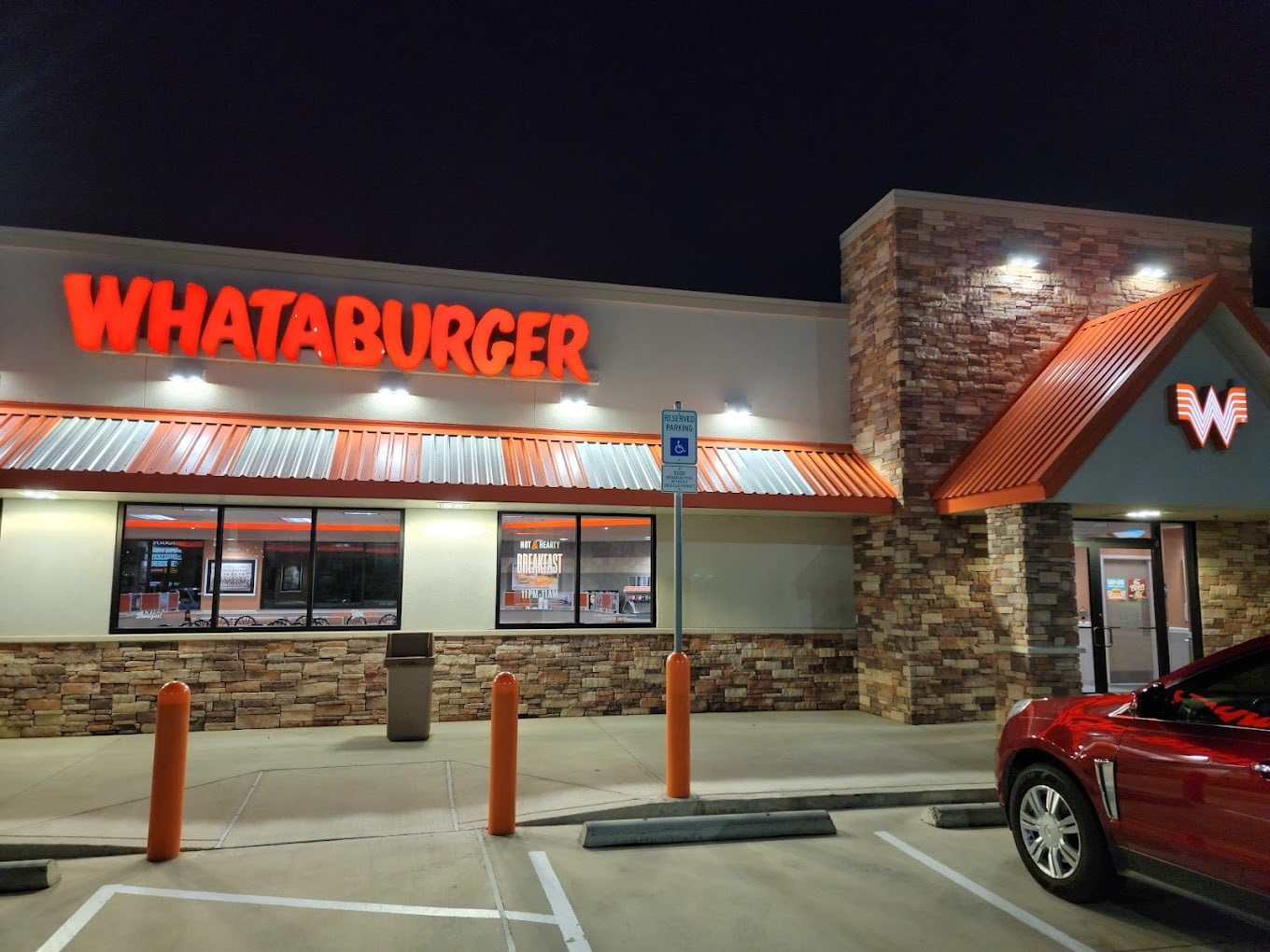A Whataburger restaurant at night with bright orange signage, stone walls, large windows, and a red car parked in front—one of the favorite fast-food chains by state. A handicap parking sign is visible near the entrance.