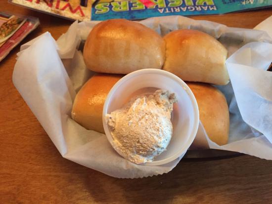 A basket with four shiny dinner rolls on parchment paper, served with a small cup of whipped cinnamon butter on the side.
