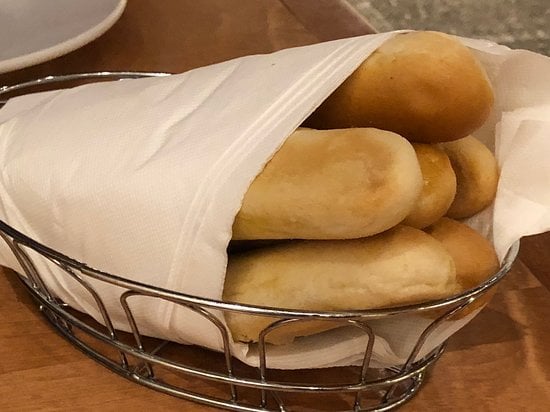Restaurants with signature dishes. A wire basket holds several golden-brown breadsticks wrapped in a white napkin, sitting on a wooden table.