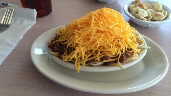 A plate of spaghetti topped with chili and a large mound of shredded cheddar cheese, served with a side of oyster crackers.