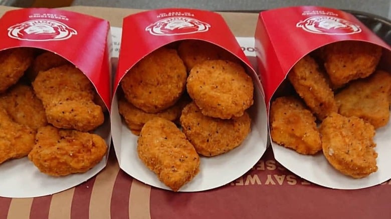 Three red paper containers filled with crispy, golden-brown chicken nuggets are lined up side by side on a brown tray liner.