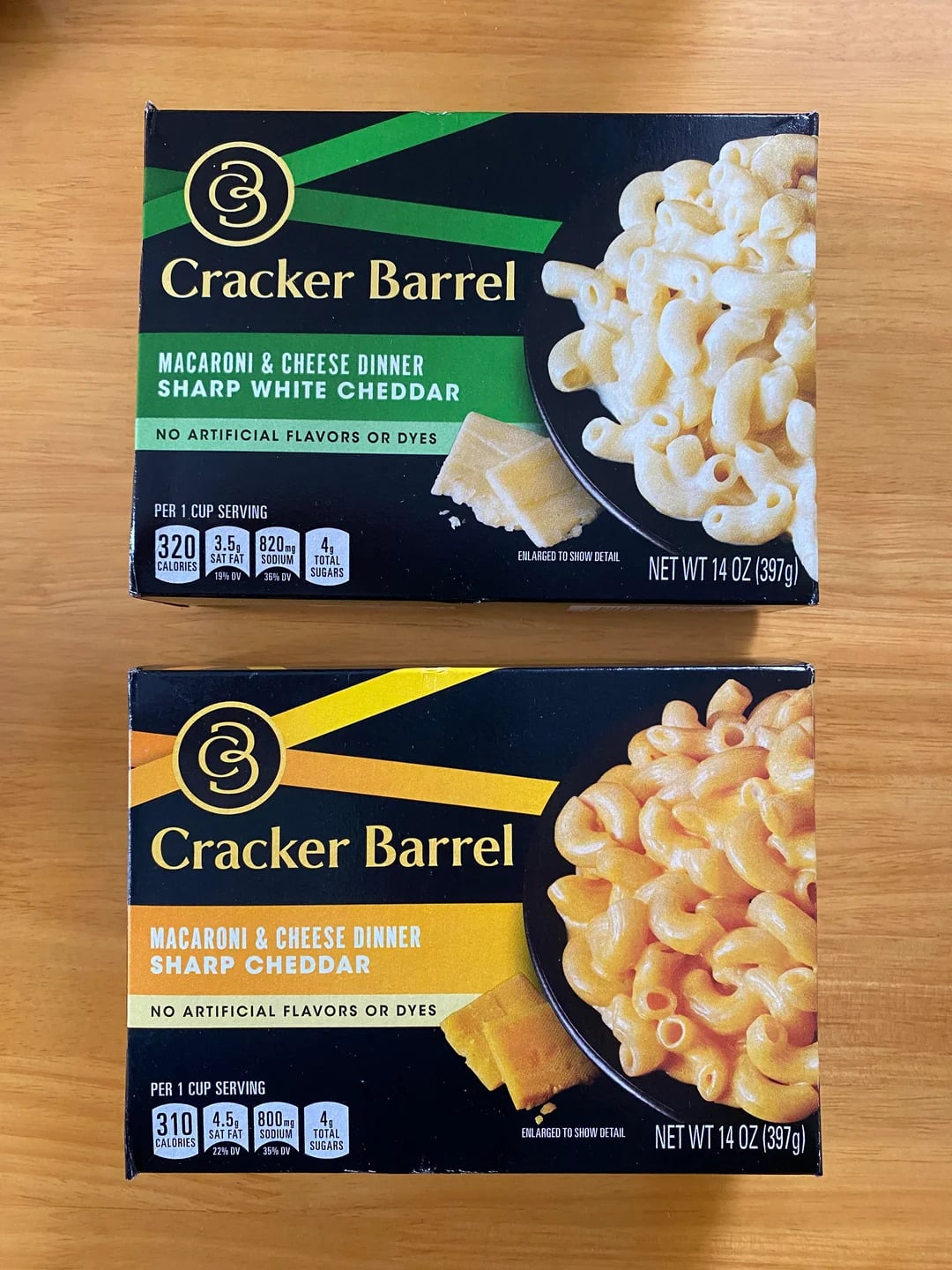 Two Cracker Barrel macaroni & cheese boxes sit on a table: one Sharp White Cheddar, the other Sharp Cheddar. Both feature appetizing macaroni and cheese images and nutrition facts on the front, highlighting the rich flavor you'd expect from a brand known for using only the best shredded cheese.