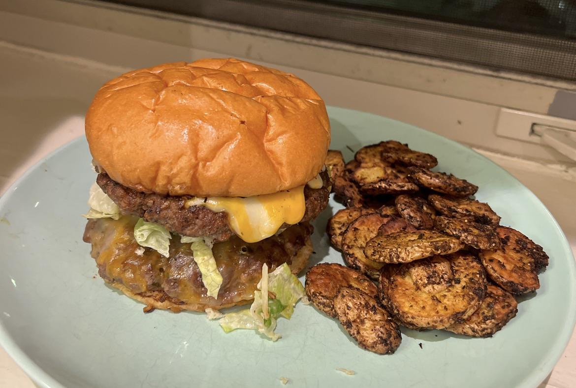 A cheeseburger with lettuce and melted cheese sits on a light blue plate next to a serving of roasted, seasoned potato slices.