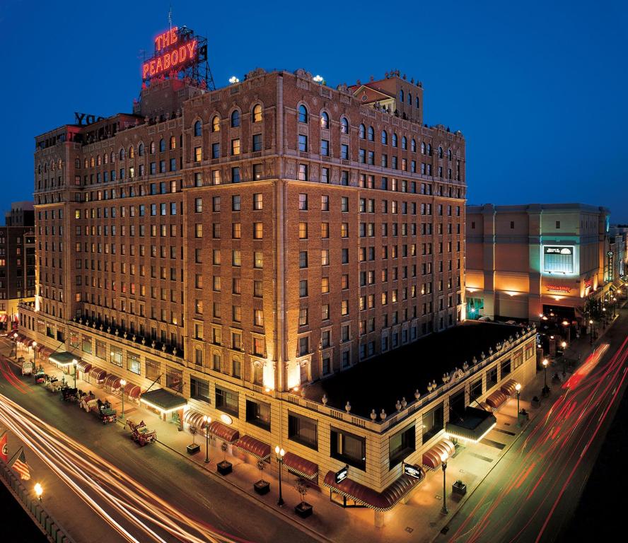 A large, historic brick hotel, “The Peabody,” stands proudly illuminated at night, embodying the grandeur of Historic Hotels. Light trails from passing cars and a glowing neon sign on the rooftop contrast beautifully against the deep blue sky.