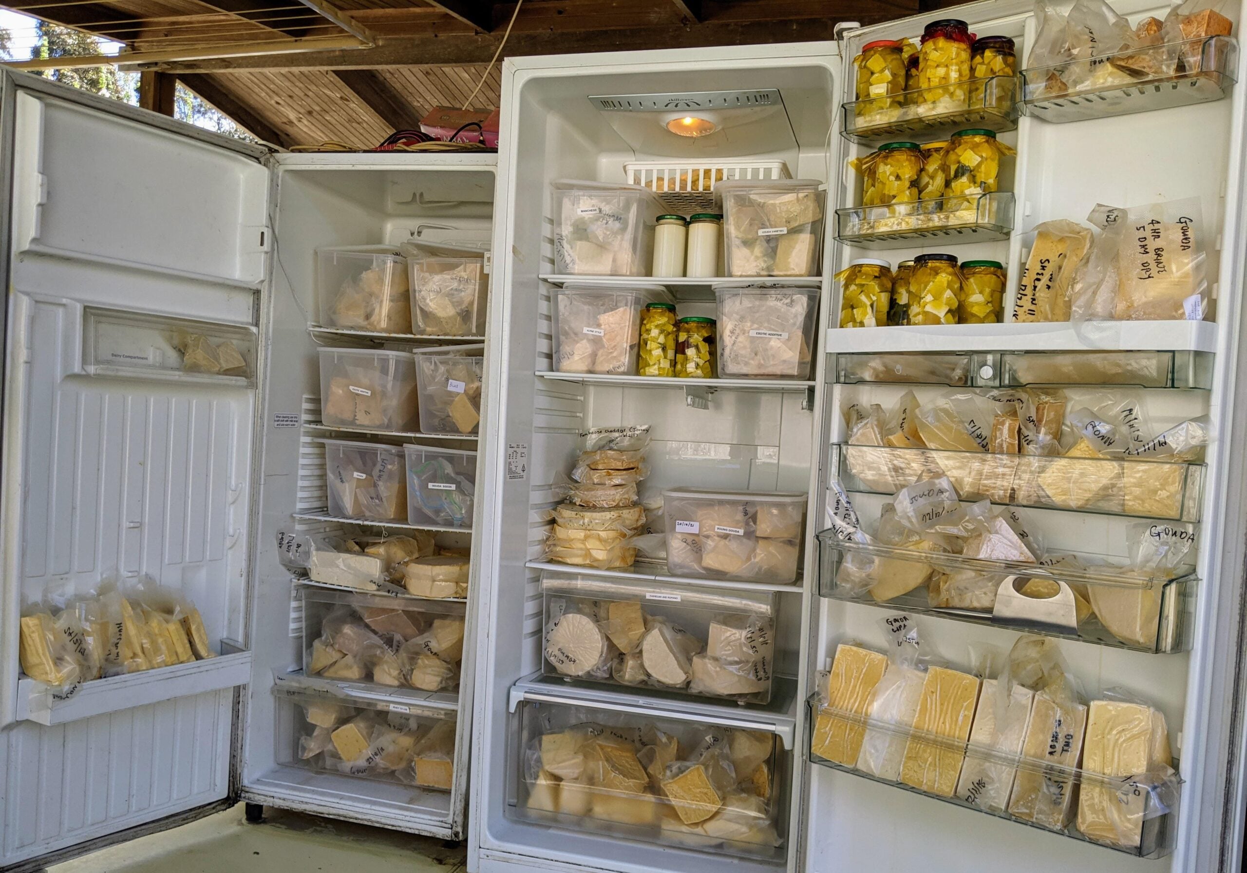An open refrigerator filled with bags and containers of cheese and jars of preserved food, neatly organized on shelves and in drawers.