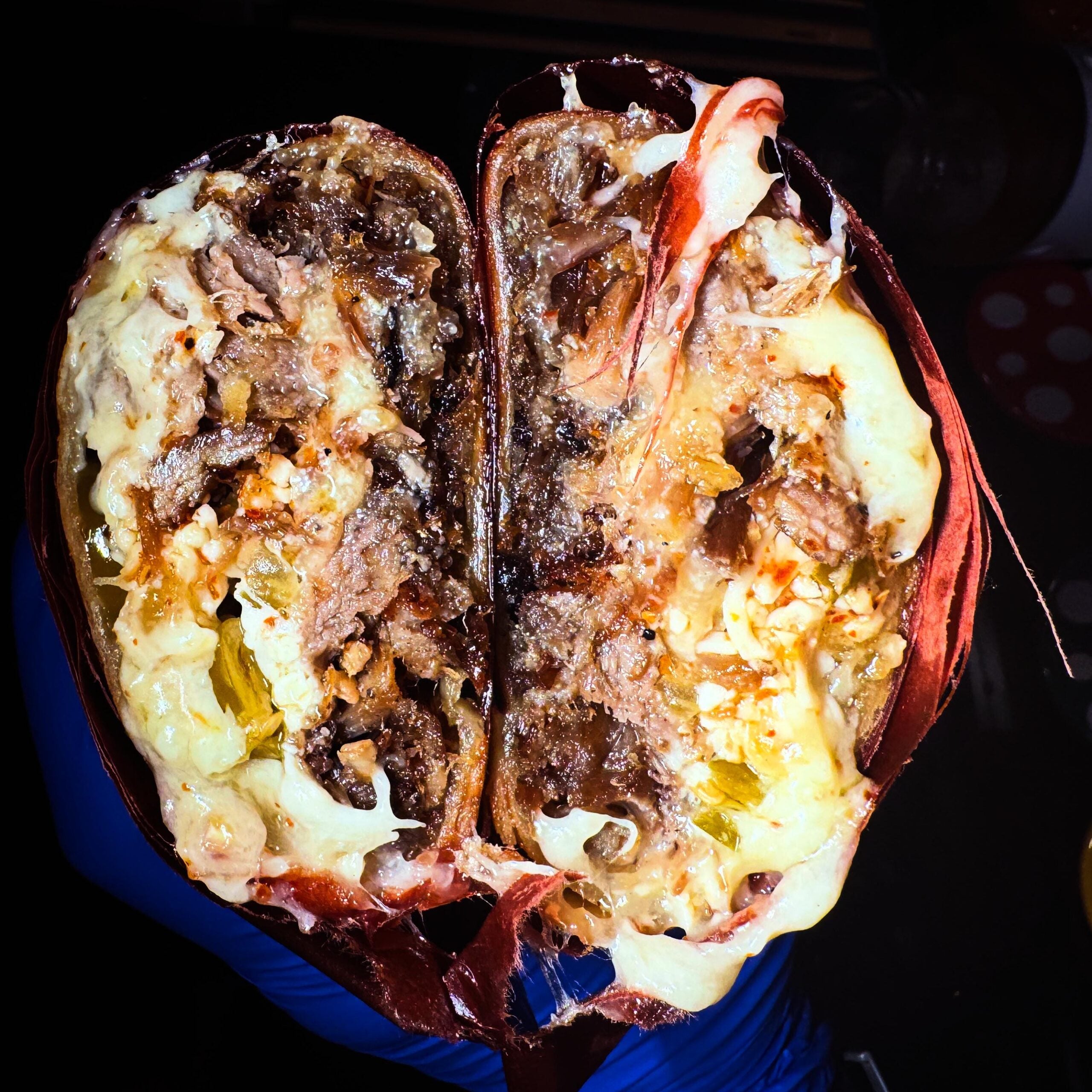 A close-up of a sliced burrito, showing melted cheese, shredded meat, lettuce, and tortilla, with the filling visibly packed inside.