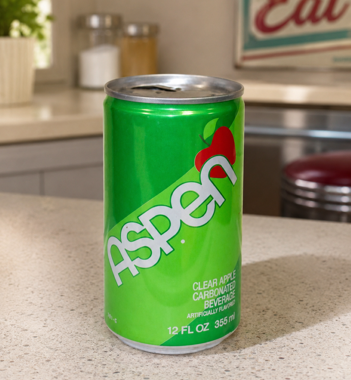 A green can of Aspen clear apple soda sits on a kitchen countertop, with a red apple graphic and vintage kitchen decor in the background, evoking memories of classic Soda Pops from days gone by.