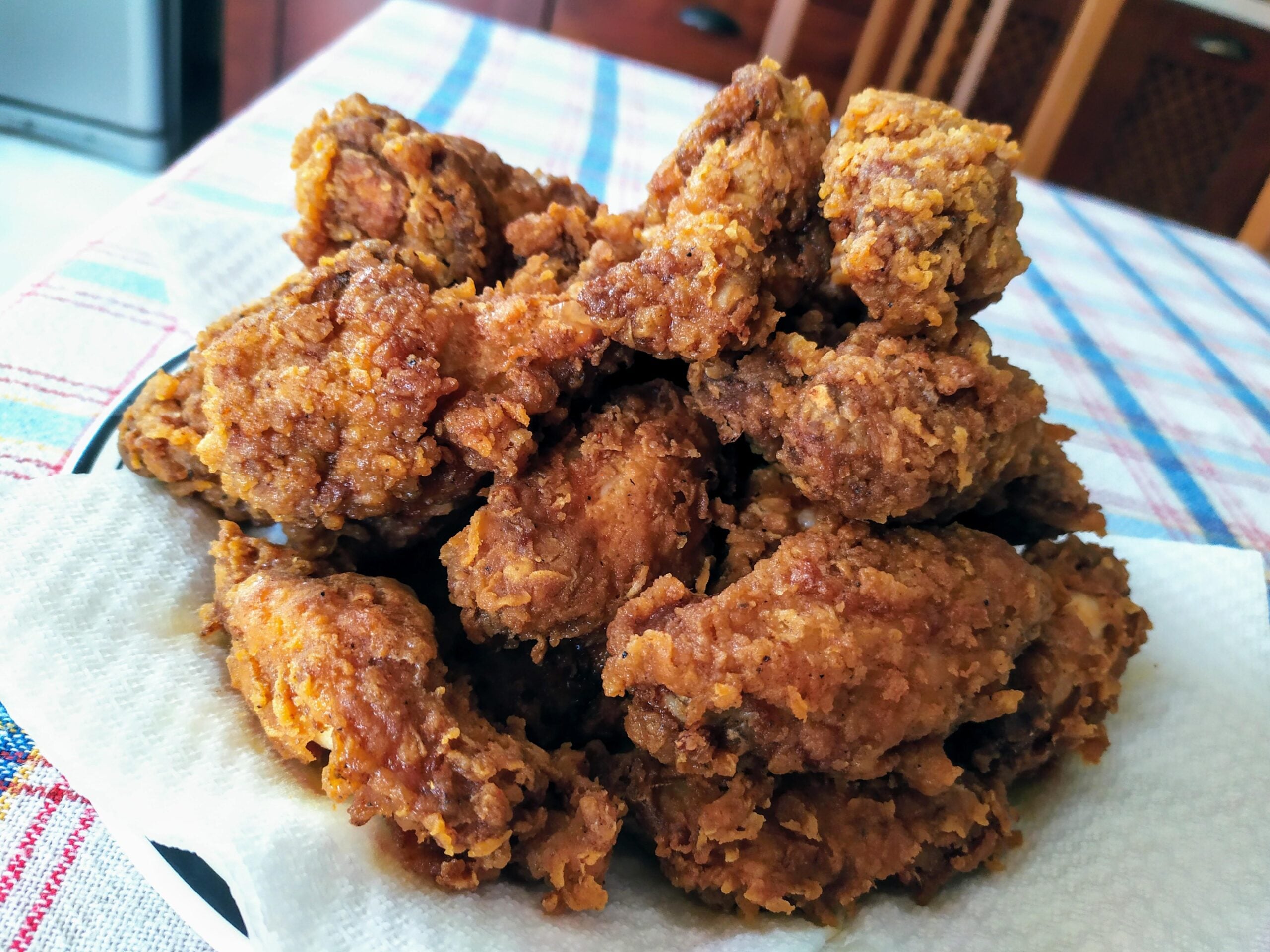 A plate piled high with crispy, golden brown fried chicken pieces sits on a white napkin atop a plaid tablecloth.