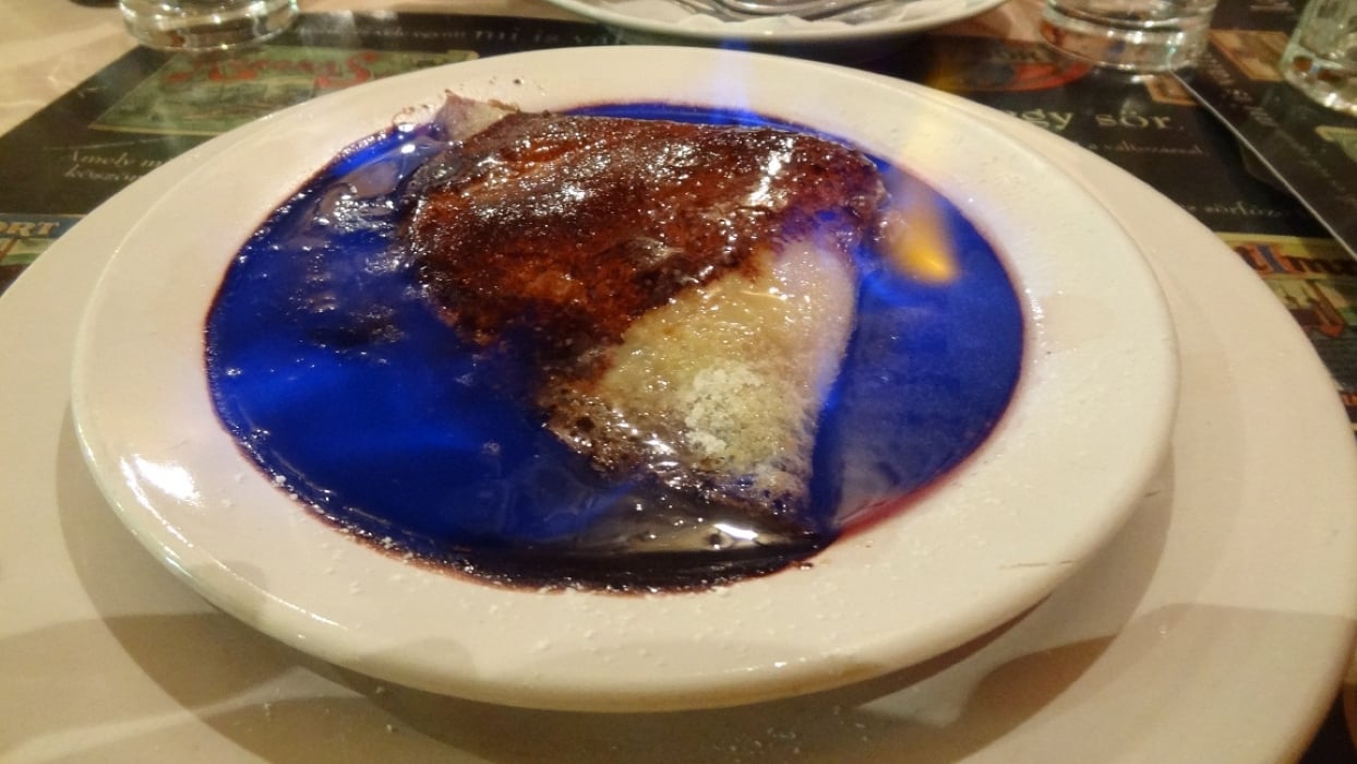 A slice of cake sits on a white plate, covered in blue flames from burning alcohol, creating a dramatic and colorful presentation—truly one of the amazing foods people ate while on vacation.