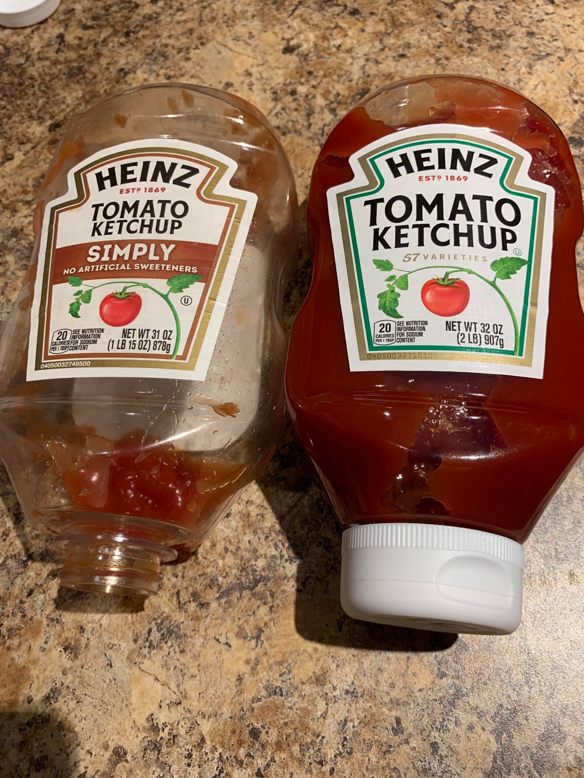 Two Heinz ketchup bottles lying on a countertop: one labeled “Simply” with little ketchup left, and the other labeled “Tomato Ketchup” is full. Both bottles are 32 oz and are placed side by side.