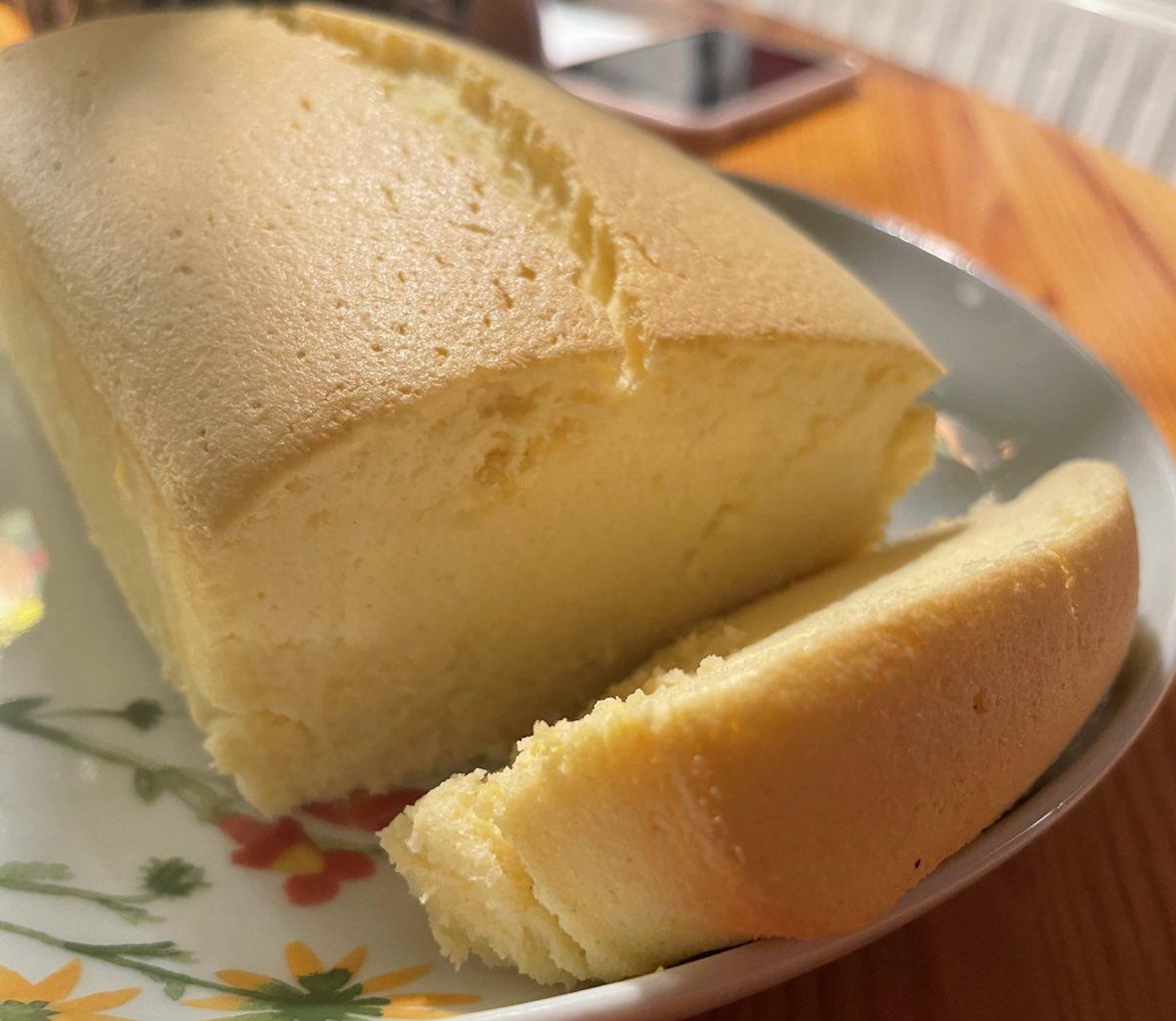 A close-up of a fluffy yellow sponge cake with a slice cut, served on a floral-patterned plate on a wooden table.