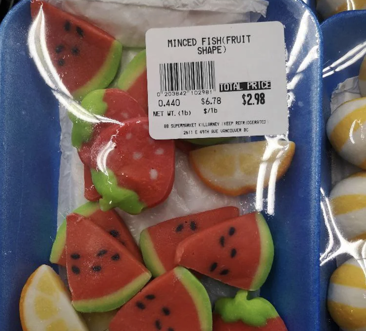 Plastic-wrapped tray with brightly colored, fruit-shaped food labeled “Minced Fish (Fruit Shape)” and priced at $2.98. The pieces resemble watermelon and lemon slices.