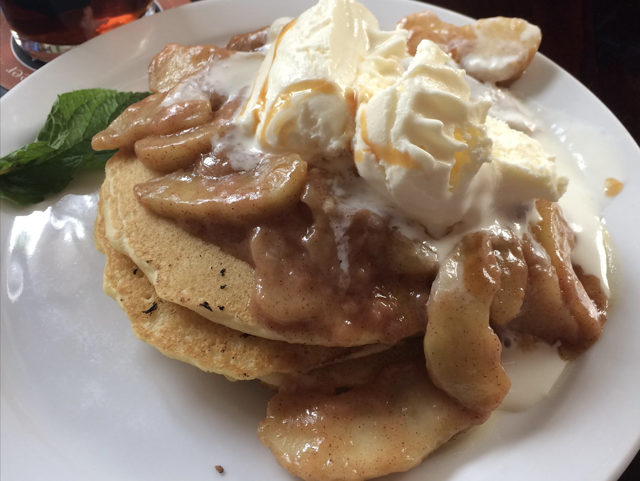 A stack of pancakes topped with caramelized apple slices and a generous scoop of melting vanilla ice cream on a white plate.