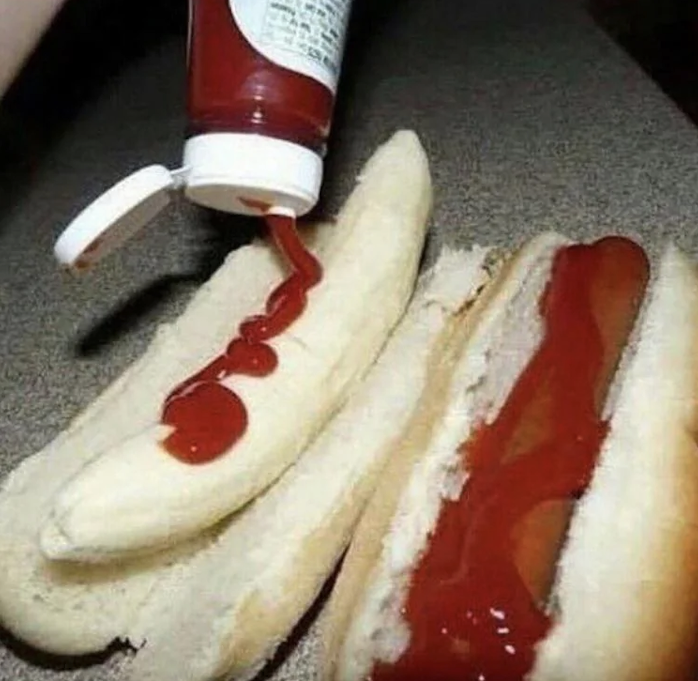 A banana in a hot dog bun is topped with ketchup next to a regular hot dog in a bun, also with ketchup.