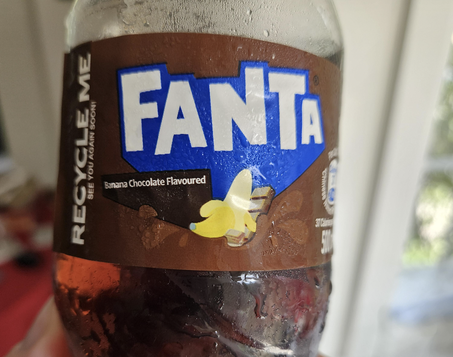A close-up of a Fanta bottle label showing a banana chocolate flavor, with images of banana slices and chocolate pieces on a brown background.