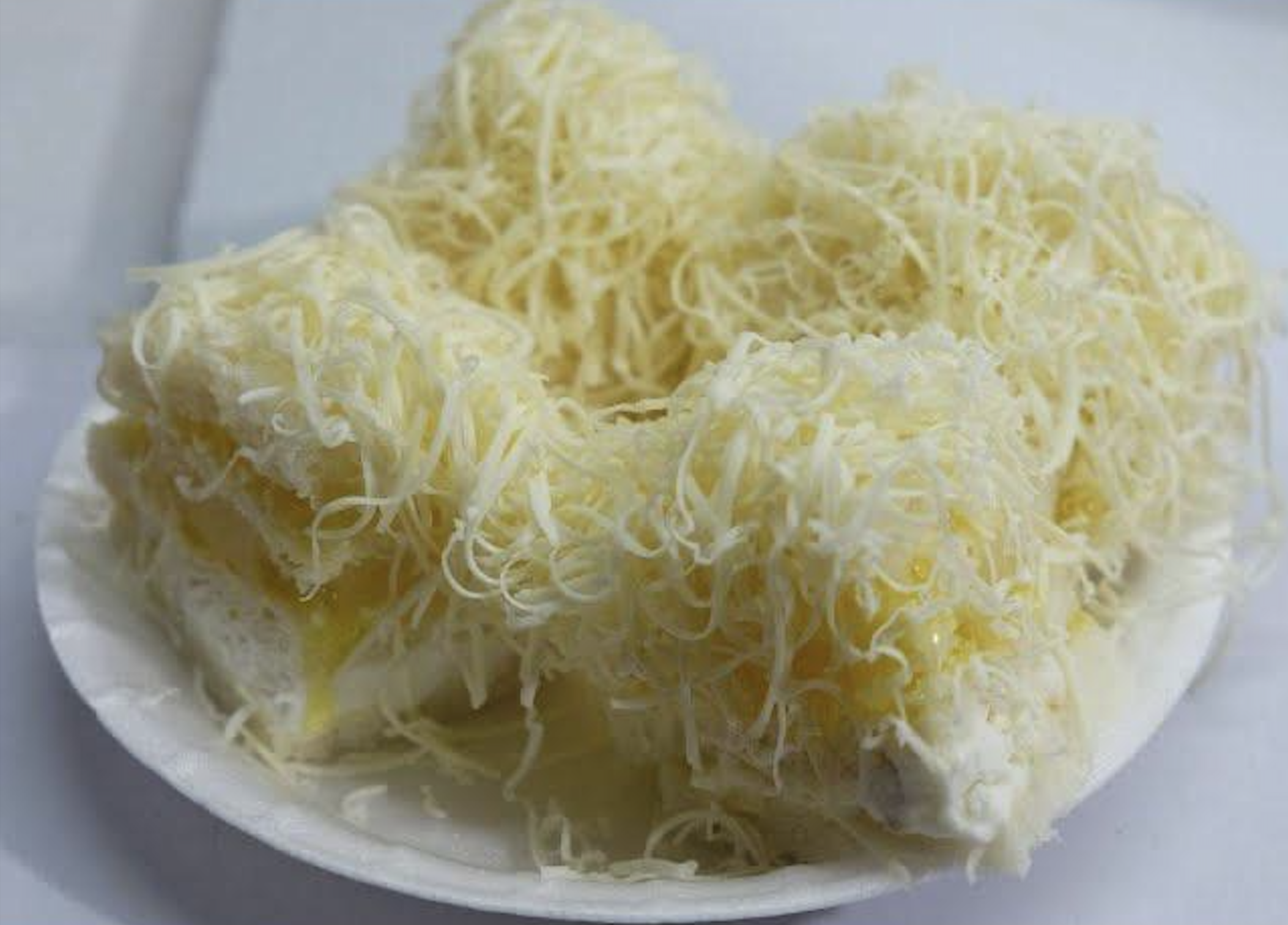 Four slices of white bread topped with layers of grated cheese and what appears to be sweet condensed milk or sauce, served on a white plate.