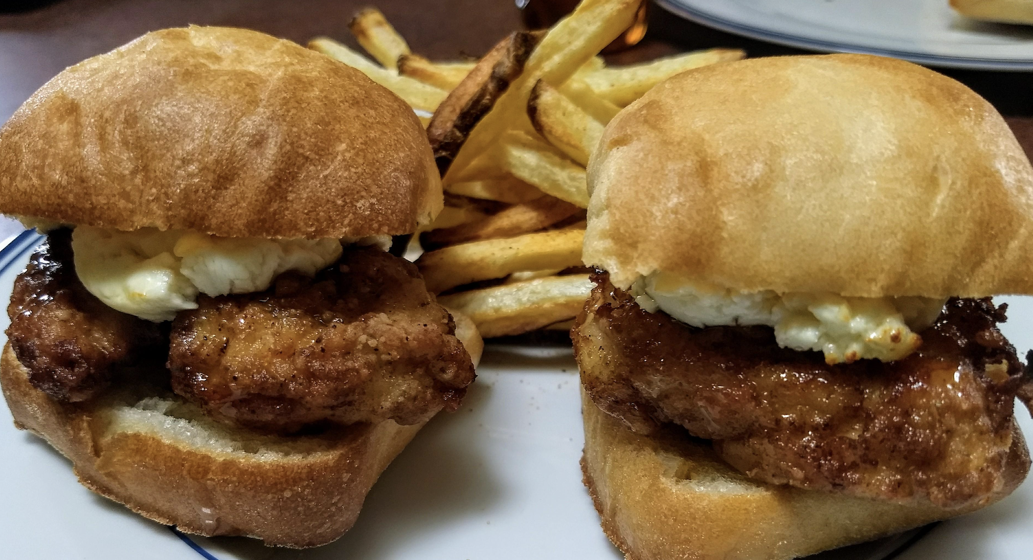 Two chicken sliders with a dollop of sauce sit on a plate next to a serving of golden French fries. The sandwiches are made with thick, crusty buns and crispy fried chicken.