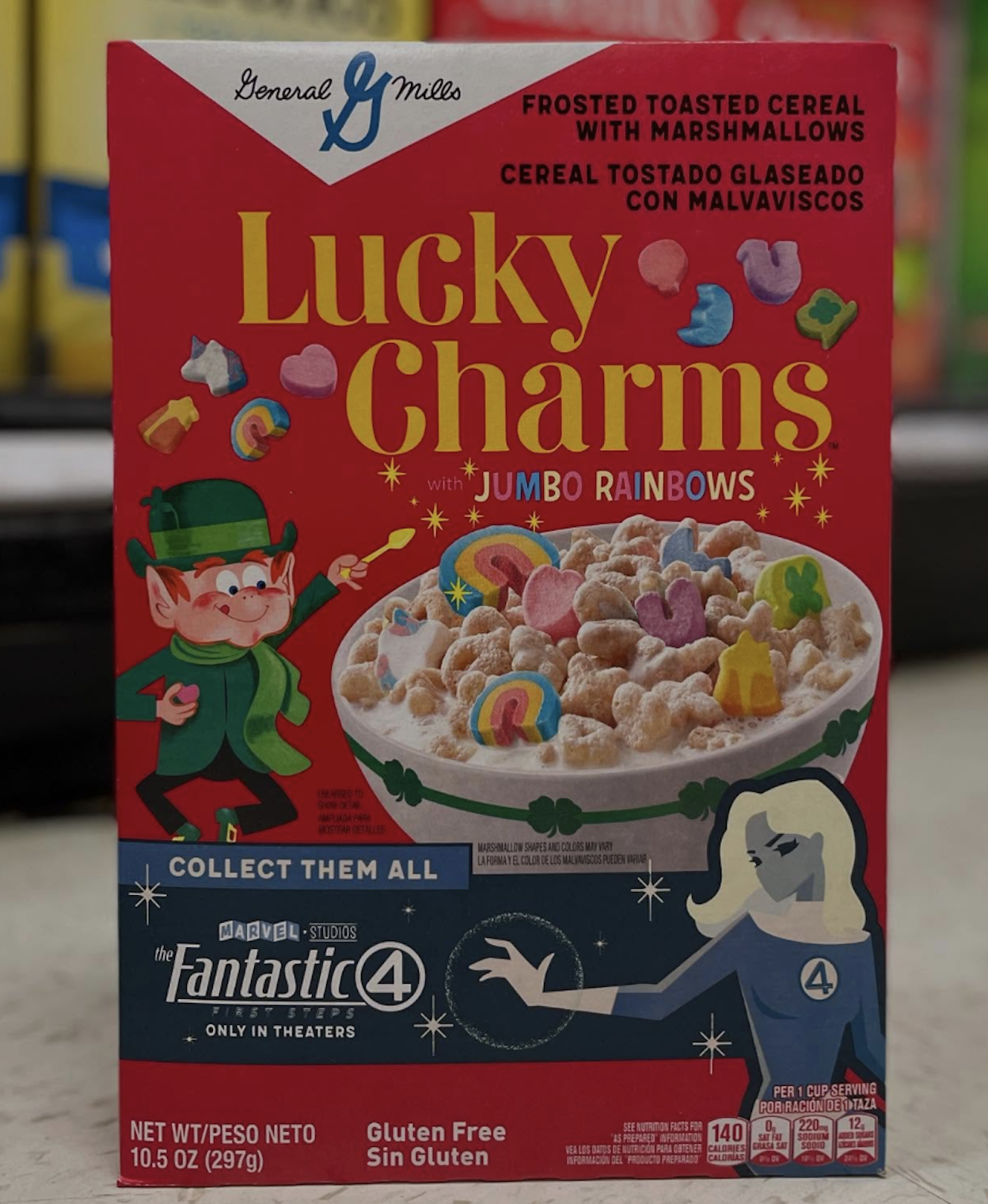 A box of Lucky Charms cereal features colorful marshmallows, a cartoon leprechaun, and Fantastic Four movie promotion on a red background. The text highlights “Jumbo Rainbows” and “Gluten Free.”